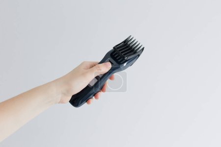 Frauenhand hält elektrische Haarschneidemaschine auf weißem Hintergrund