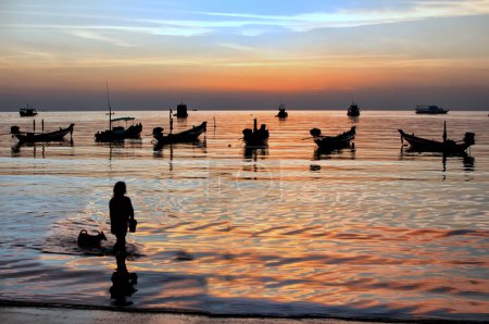 Téléchargez les photos : Silhouette des bateaux à longue queue avec fille locale et chien au coucher du soleil à Sairee Beach, Koh Tao, Thaïlande - en image libre de droit