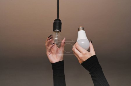 Téléchargez les photos : Incandescent and LED lamps are in women's hands. Replacement of the lamp in the cartridge. - en image libre de droit