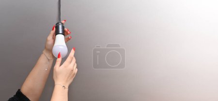 Téléchargez les photos : Les mains des femmes avec une manucure rouge visser une lampe LED électrique dans la cartouche. Gros plan. bannière. - en image libre de droit
