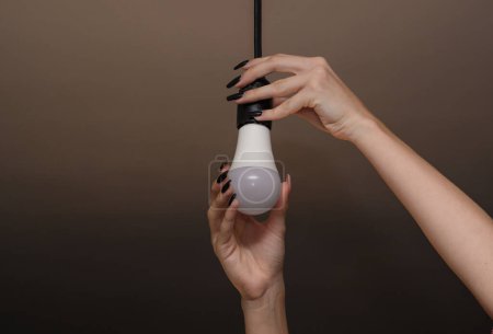 Téléchargez les photos : Women's hands screw in a light bulb. led lamp - en image libre de droit
