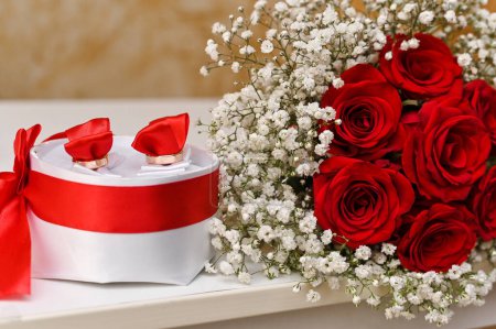 a bouquet of red roses and a gift in a box with red ribbons
