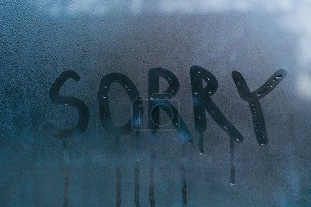 The word sorry is written on the wet glass of the window. 