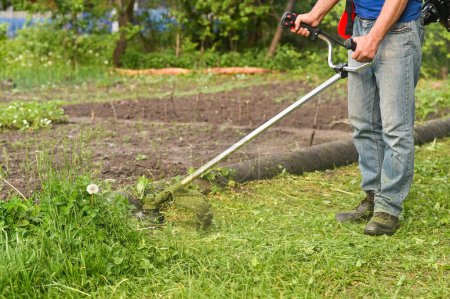 Mann mäht hohes Gras mit Rasentrimmer im Hinterhof. Werkzeuge und Geräte für die Gartenpflege. Rasentrimmen mit Benzinhandmäher