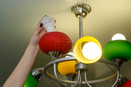 A woman's hand screws an LED lamp into a chandelier.