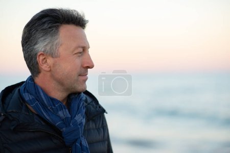 Foto de Hombre maduro guapo en la playa, retrato al aire libre. Atractivo feliz sonriente modelo masculino adulto posando a la orilla del mar, al atardecer o al amanecer - Imagen libre de derechos