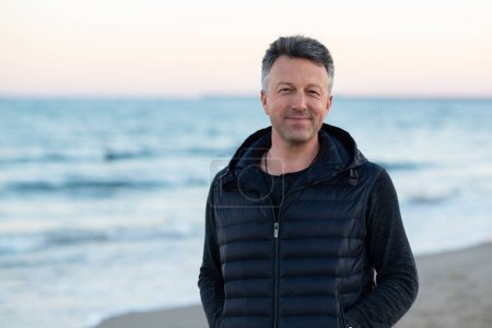 Photo for Handsome mature man at the beach, outdoor portrait. Attractive happy smiling adult male model posing at seaside, sunset or sunrise time - Royalty Free Image