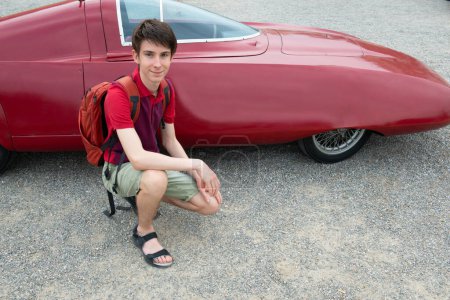 Téléchargez les photos : Beau gai adolescent garçon près rétro course rouge voiture en plein air, détail - en image libre de droit