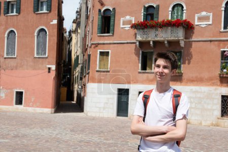 Téléchargez les photos : Beau garçon adolescent joyeux posant dans les rues de l'ancienne Venise avec de beaux bâtiments en été - en image libre de droit