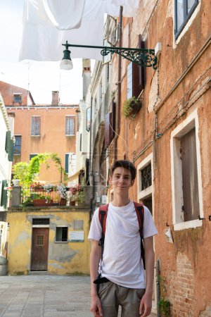 Téléchargez les photos : Beau sourire adolescent garçon posant sur lavage sont séchés accrochés sur des cordes à linge dans les rues de l'ancienne Venise - en image libre de droit