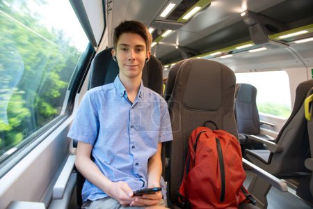 Photo for Handsome cheerful teen boy riding a train and using a smartphone - Royalty Free Image