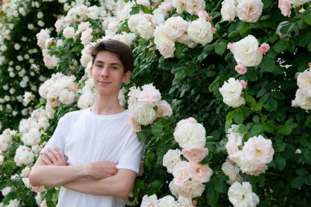 Téléchargez les photos : Adolescent garçon dans parc parmi belle blanc-rose floraison roses été en plein air - en image libre de droit