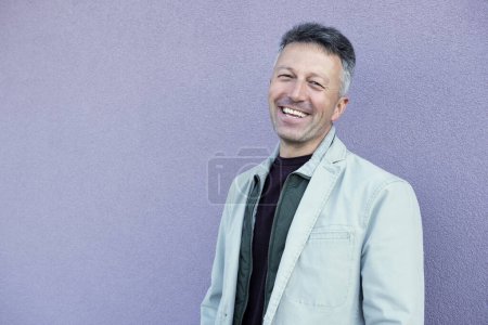 Téléchargez les photos : Homme d'âge moyen posant au-dessus de lilas wal. Un bel homme mûr. Portrait masculin extérieur. - en image libre de droit