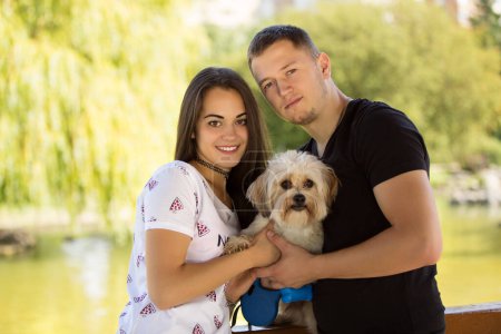 Photo for Young couple with puppy. Portrait of attractive happy smiling young woman and man holding cute little dog, summer park outdoor. - Royalty Free Image