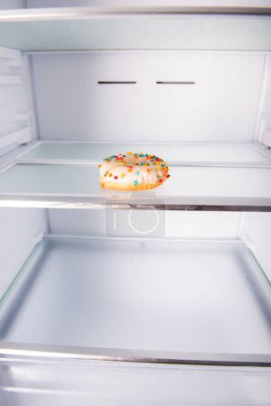 Téléchargez les photos : Réfrigérateur vide ouvert avec un beignet sur l'étagère, concept de régime - en image libre de droit