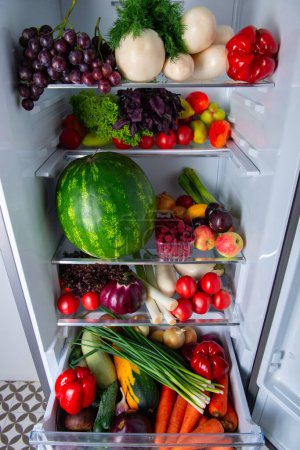 Foto de Nevera abierta llena de verduras y frutas frescas maduras de temporada. El concepto de dieta, alimentación saludable y vegetarianismo - Imagen libre de derechos
