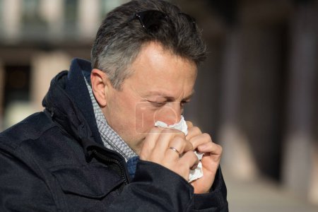 Photo for Handsome man with cold in the head. Outdoor winter male portrait. Attractive confident middle-aged man blow his nose over city buildings - Royalty Free Image
