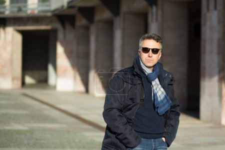 Téléchargez les photos : Un bel homme. Portrait masculin d'hiver extérieur. attrayant confiant homme d'âge moyen en lunettes de soleil posant sur les bâtiments de la ville - en image libre de droit