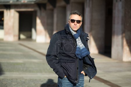 Photo for Handsome man. Outdoor winter male portrait. Attractive confident middle-aged man in sunglasses posing over city buildings - Royalty Free Image