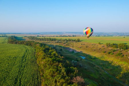 Téléchargez les photos : La montgolfière vole dans le ciel au-dessus des champs, prairies, arbres et ravins le matin - en image libre de droit
