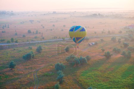 Foto de Globo de aire caliente está volando sobre el prado temprano en la mañana brumosa al amanecer - Imagen libre de derechos