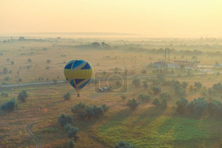 Photo for Hot air balloon is flying over meadow early foggy morning at sunrise - Royalty Free Image