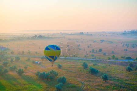Téléchargez les photos : La montgolfière vole au-dessus du pré tôt le matin brumeux au lever du soleil - en image libre de droit