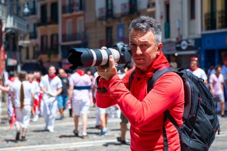 Téléchargez les photos : Photographe à San Fermin. Photojournaliste. Les gens célèbrent le festival San Fermin dans des vêtements blancs et rouges traditionnels avec cravate rouge, Pampelune, Navarre, Espagne - en image libre de droit