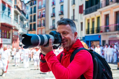 Téléchargez les photos : Photographe à San Fermin. Photojournaliste. Les gens célèbrent le festival San Fermin dans des vêtements blancs et rouges traditionnels avec cravate rouge, Pampelune, Navarre, Espagne. - en image libre de droit