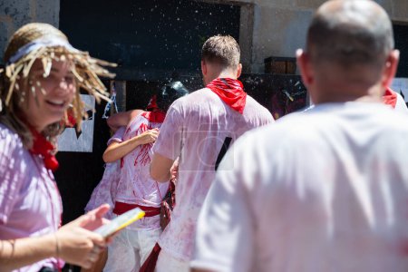 Foto de La gente rociada con vino y agua celebra la fiesta de San Fermín con ropa roja tradicional de abd blanco con corbata roja en Pamplona, Navarra, España - Imagen libre de derechos