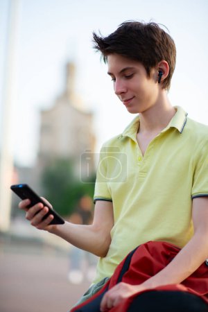 Photo for Young boy using smartphone over summer city outdoor. 15 years old teenager talking and sends messages by mobile phone, urban youth lifestyle - Royalty Free Image