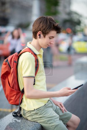 Téléchargez les photos : Jeune garçon utilisant smartphone sur la ville d'été en plein air. 15 ans adolescent parler et envoie des messages par téléphone mobile, mode de vie de la jeunesse urbaine - en image libre de droit