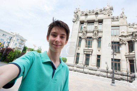 Photo for Young handsome teen boy looking at camera and happy smiling takes a selfie with smartphone over Bankova street, summer city center of Kyiv, Ukraine - Royalty Free Image