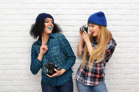 Foto de Dos chicas divertidas felices tomando fotos con cámaras retro sobre la pared blanca - Imagen libre de derechos