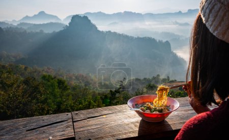 Turista asiática comiendo fideos mientras mira la nebulosa vista de la montaña. viajar en Mae Hong Son, Tailandia