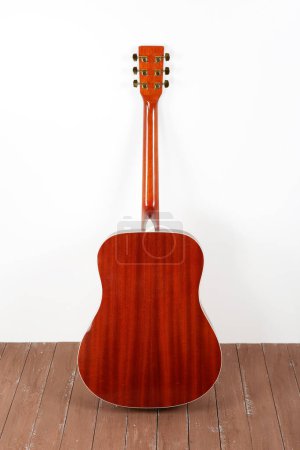 Photo for Musical instrument - back view classic acoustic guitar on a white wall background and wooden floor. - Royalty Free Image