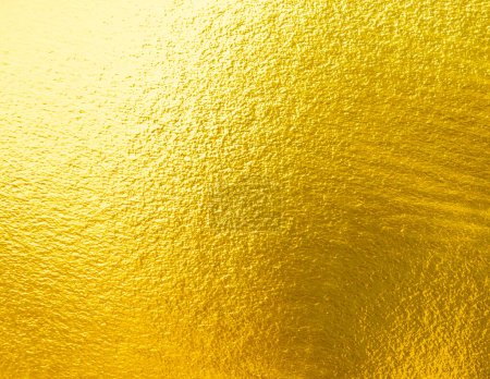 Gold wall texture background. Yellow shiny gold foil paint on wall sheet with gloss light reflection, vibrant golden paper luxury wallpaper