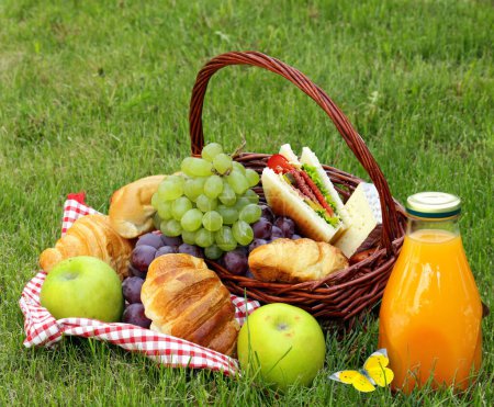 Foto de Cesta con frutas y comida de picnic en césped verde - Imagen libre de derechos