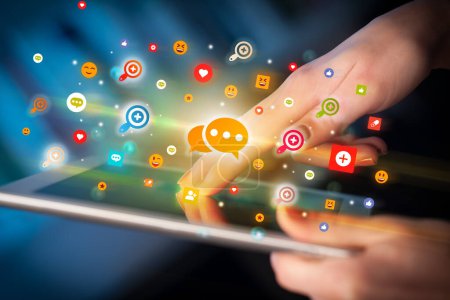 Foto de Primer plano de una mano usando tableta con iconos de mensajería de colores que salen de ella, concepto de redes sociales - Imagen libre de derechos