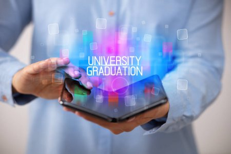 Photo for Young man holding a foldable smartphone with UNIVERSITY GRADUATION inscription, educational concept - Royalty Free Image