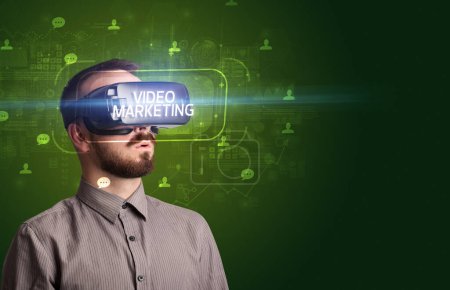 Téléchargez les photos : Homme d'affaires regardant à travers des lunettes de réalité virtuelle avec inscription VIDEO MARKETING, concept de réseau social - en image libre de droit