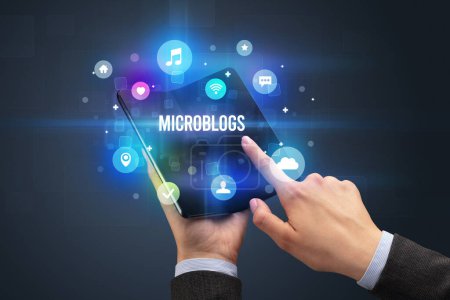 Foto de Empresario sosteniendo un smartphone plegable con inscripción MICROBLOGS, concepto de redes sociales - Imagen libre de derechos
