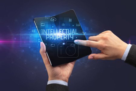 Foto de Empresario sosteniendo un smartphone plegable con inscripción PROPIEDAD INTELECTUAL, concepto de ciberseguridad - Imagen libre de derechos
