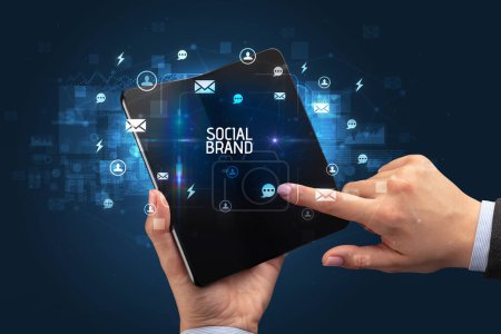 Foto de Empresario sosteniendo un smartphone plegable con inscripción SOCIAL BRAND, concepto de redes sociales - Imagen libre de derechos