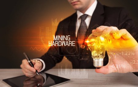 Foto de Empresario sosteniendo bombilla con inscripción MINING HARDWARE, concepto de tecnología empresarial - Imagen libre de derechos