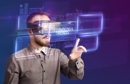 Téléchargez les photos : Homme d'affaires regardant à travers des lunettes de réalité virtuelle avec inscription TECHNOLOGIE TENDANCES, nouveau concept technologique - en image libre de droit