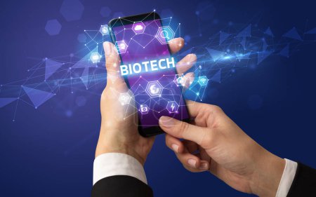 Photo for Female hand holding smartphone with BIOTECH inscription, modern technology concept - Royalty Free Image