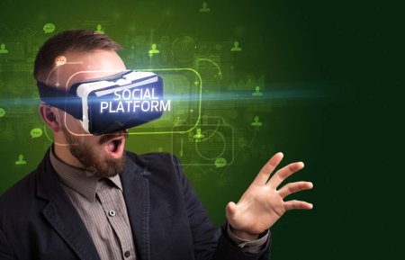 Téléchargez les photos : Homme d'affaires regardant à travers des lunettes de réalité virtuelle avec inscription PLATEFORME SOCIALE, concept de réseautage social - en image libre de droit