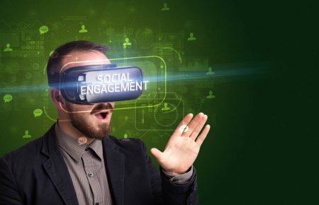 Téléchargez les photos : Homme d'affaires regardant à travers des lunettes de réalité virtuelle avec inscription ENGAGEMENT SOCIAL, concept de réseautage social - en image libre de droit