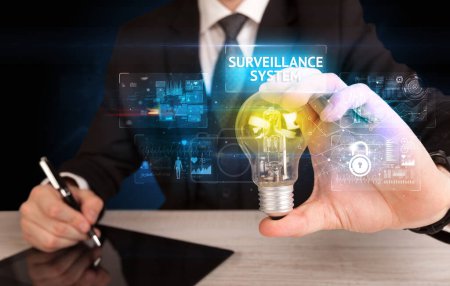 Foto de Empresario sosteniendo bombilla con inscripción SISTEMA DE VIGILANCIA, concepto de idea de seguridad en línea - Imagen libre de derechos
